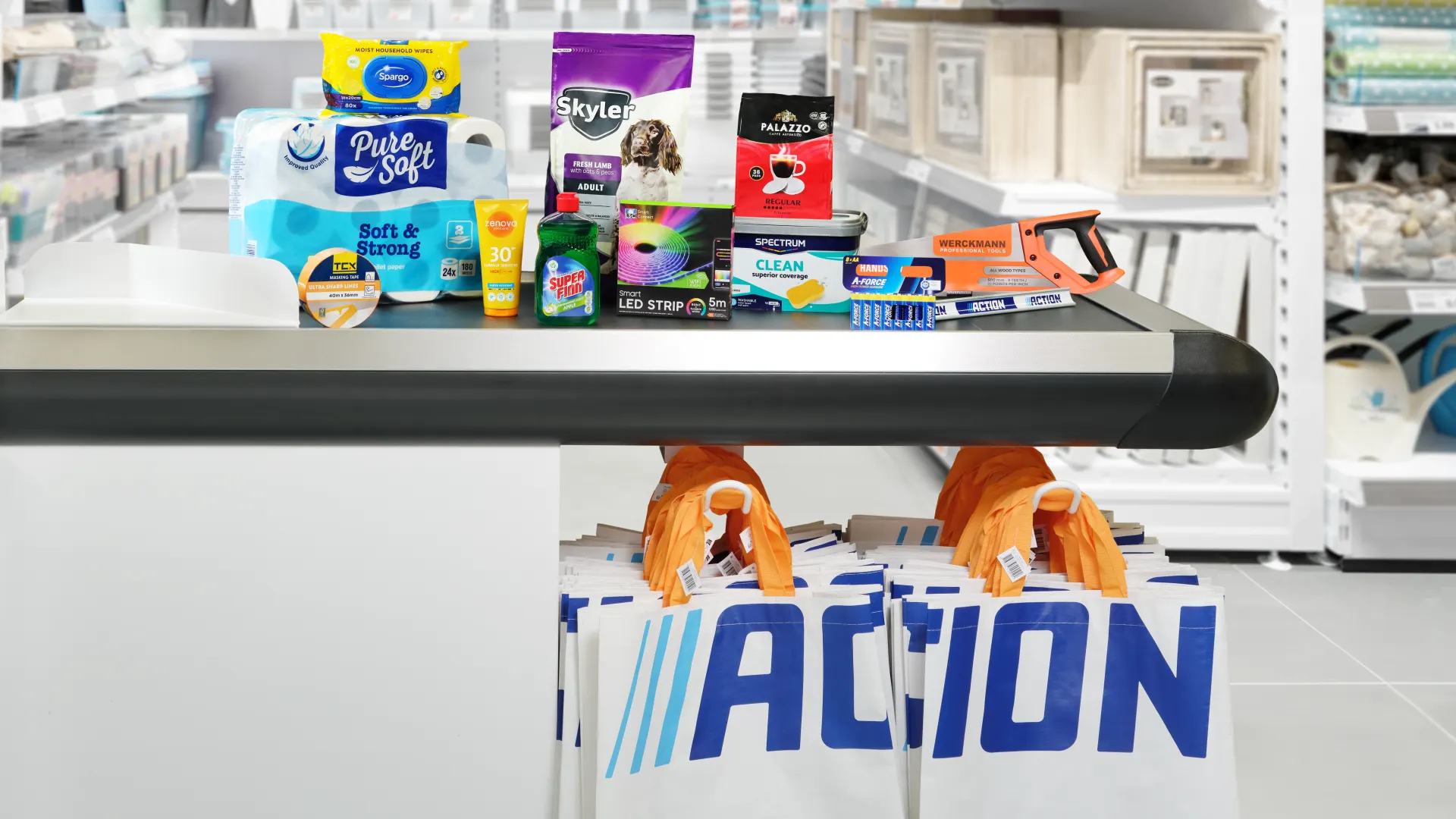 Produtos variados da Action numa caixa de supermercado com sacos da marca