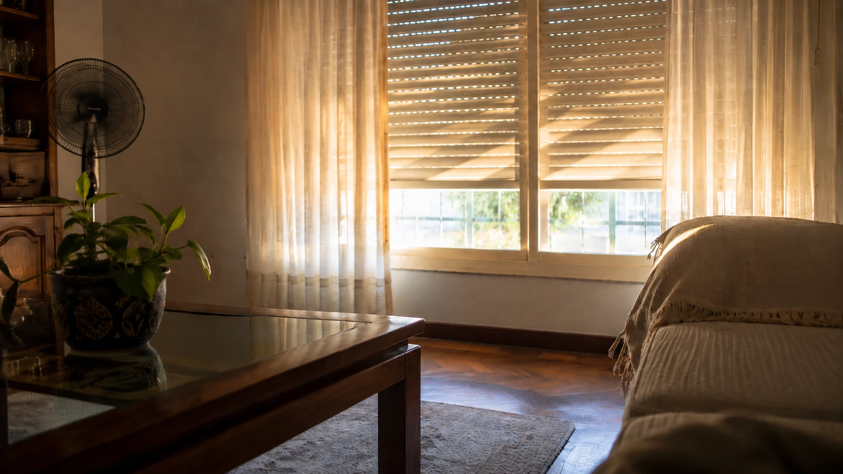 Sala com estores parcialmente fechados e ventoinha durante uma tarde quente de verão.